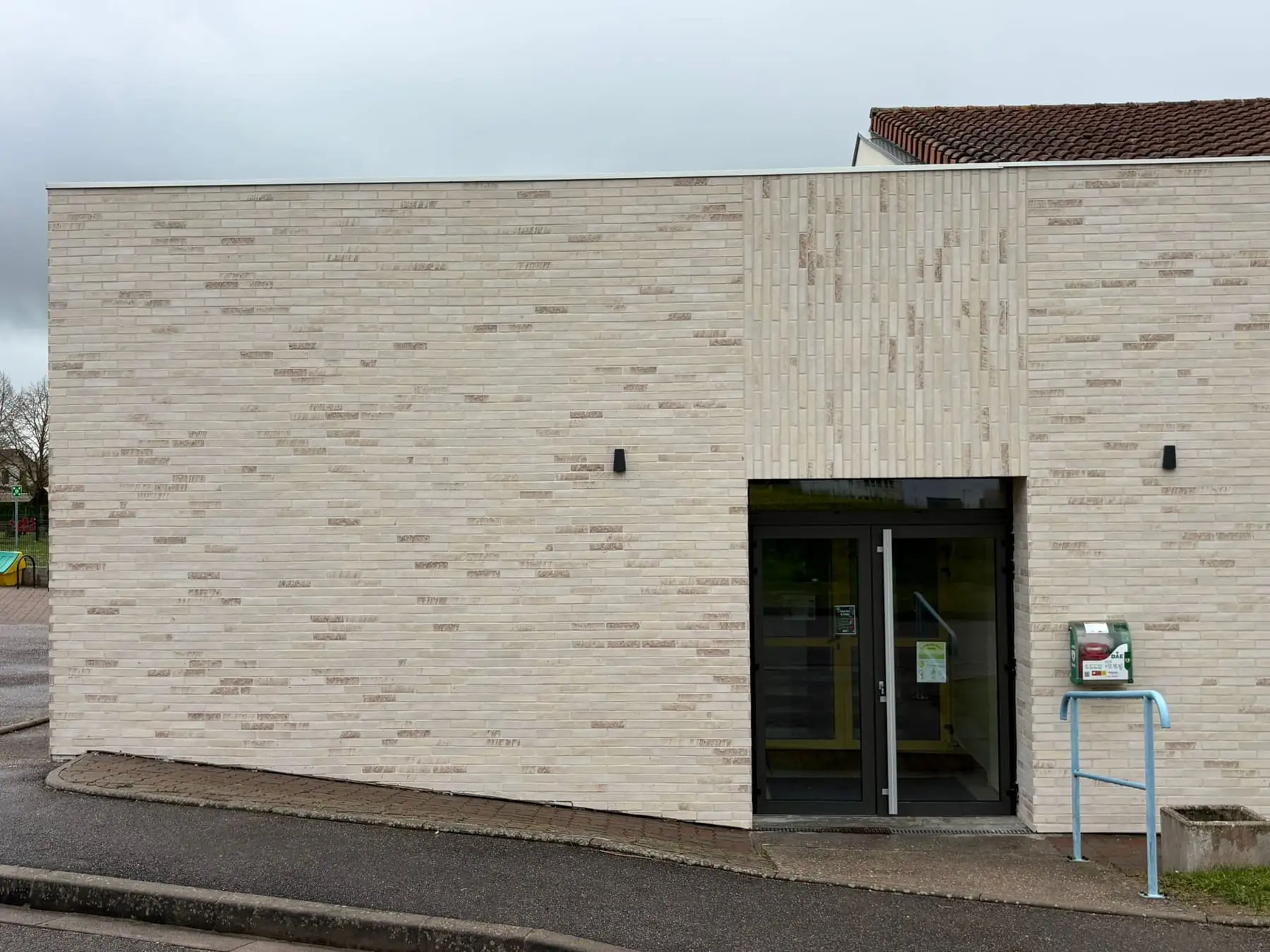 Entrée vitrée encadrée d’un panneau de plaquettes posées à la verticale, le reste de la façade en pose horizontale.