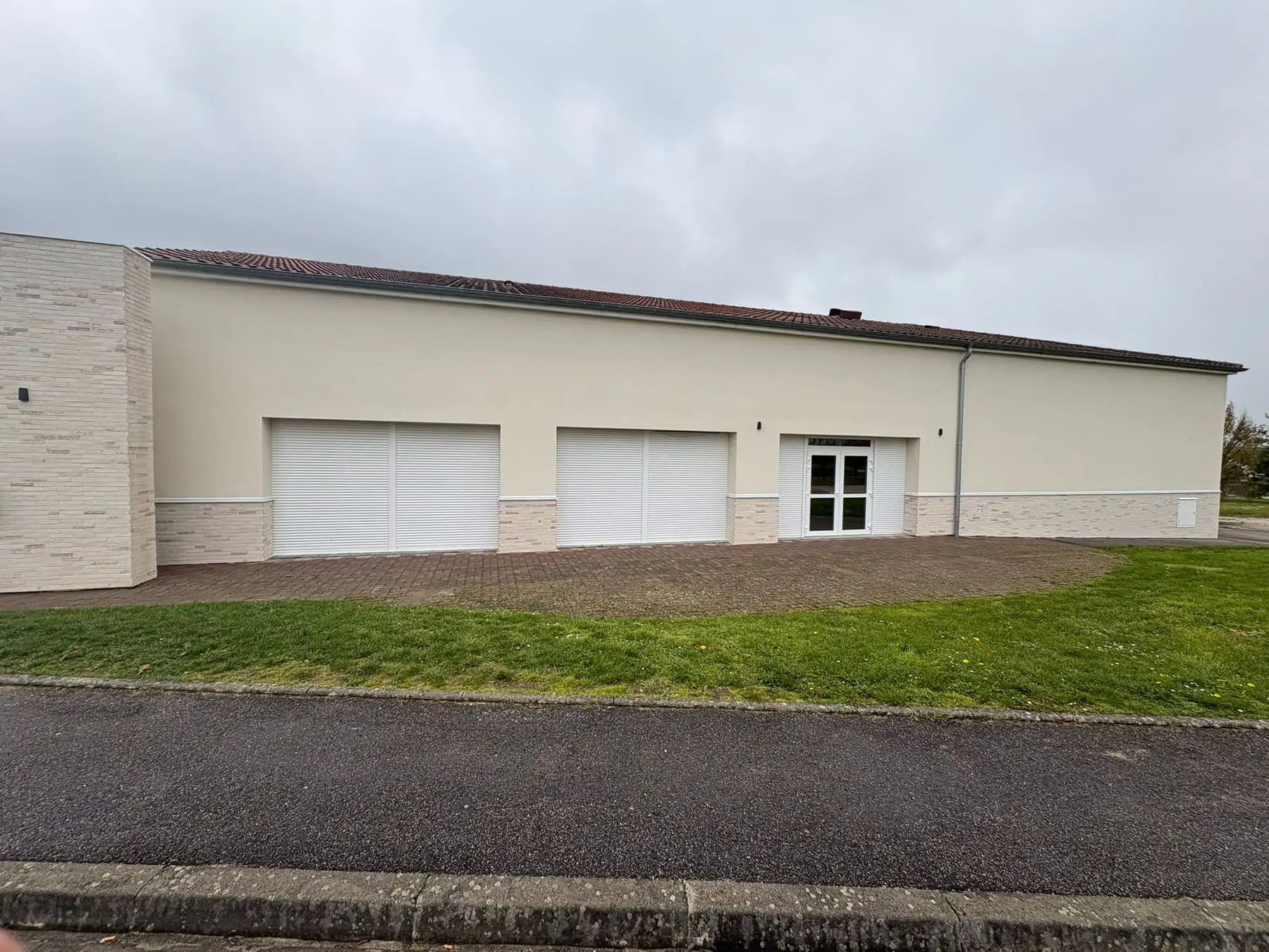 Façade arrière enduite beige avec un soubassement en plaquettes claires et trois grandes baies à volets roulants blancs.