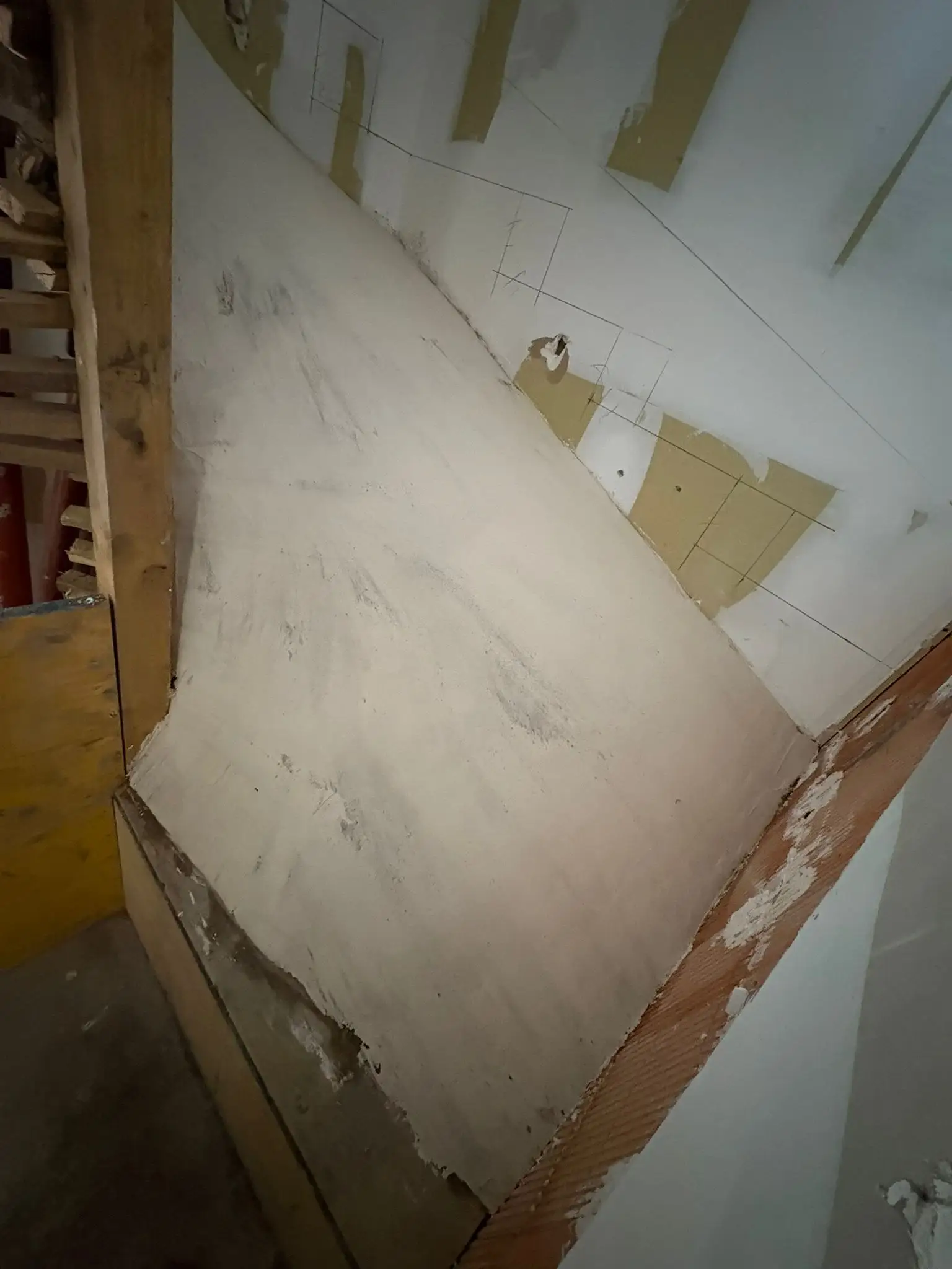 Surface de mortier lissée dans une pièce en rénovation, bordée d’une cloison en plaques de plâtre et d’un montant en bois.