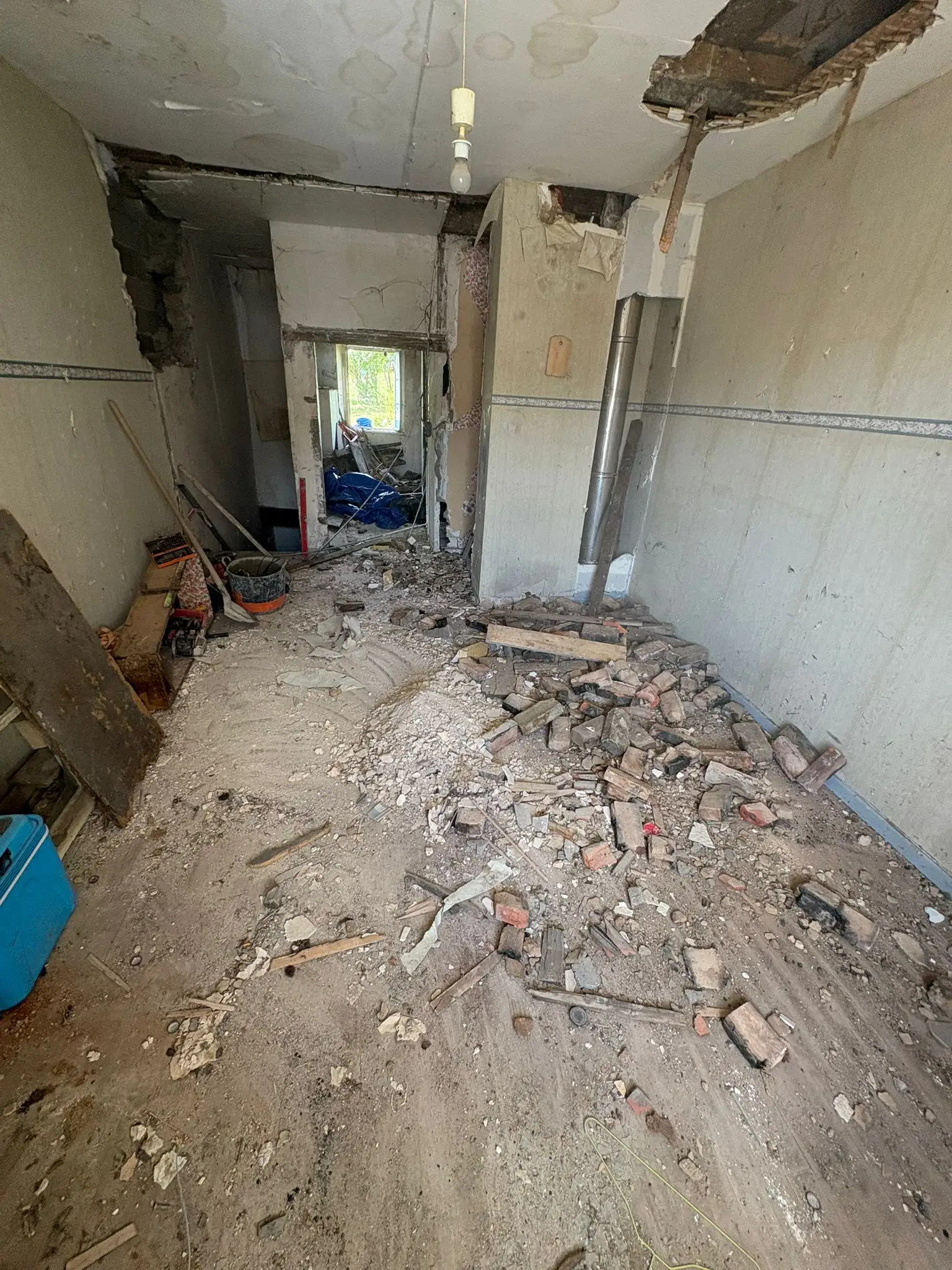 Pièce en cours de démolition intérieure, gravats de briques au sol, cloison ouverte et conduit apparent.