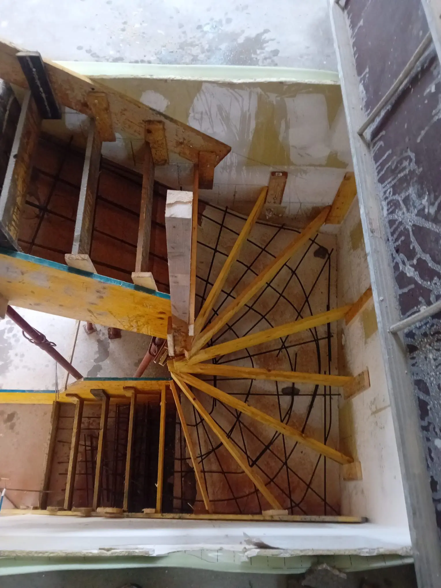Vue plongeante dans une cage d’escalier montrant le coffrage bois en éventail et le ferraillage d’un escalier béton avant coulage.
