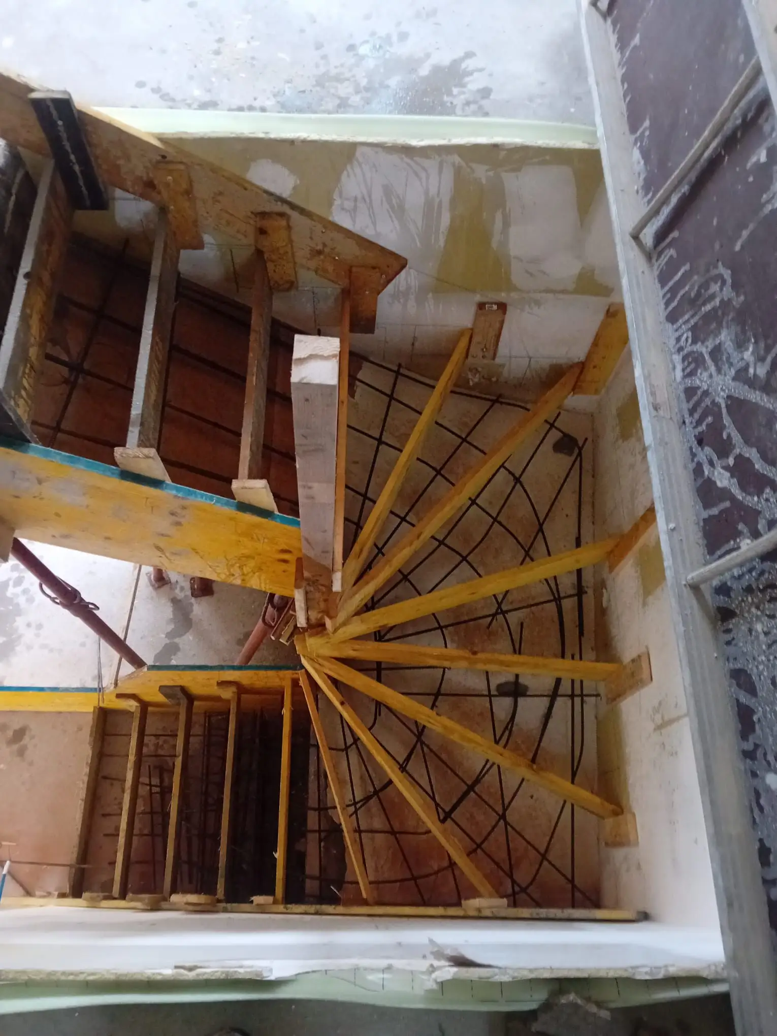 Vue plongeante dans une cage d’escalier montrant le coffrage bois en éventail et le ferraillage d’un escalier béton avant coulage.