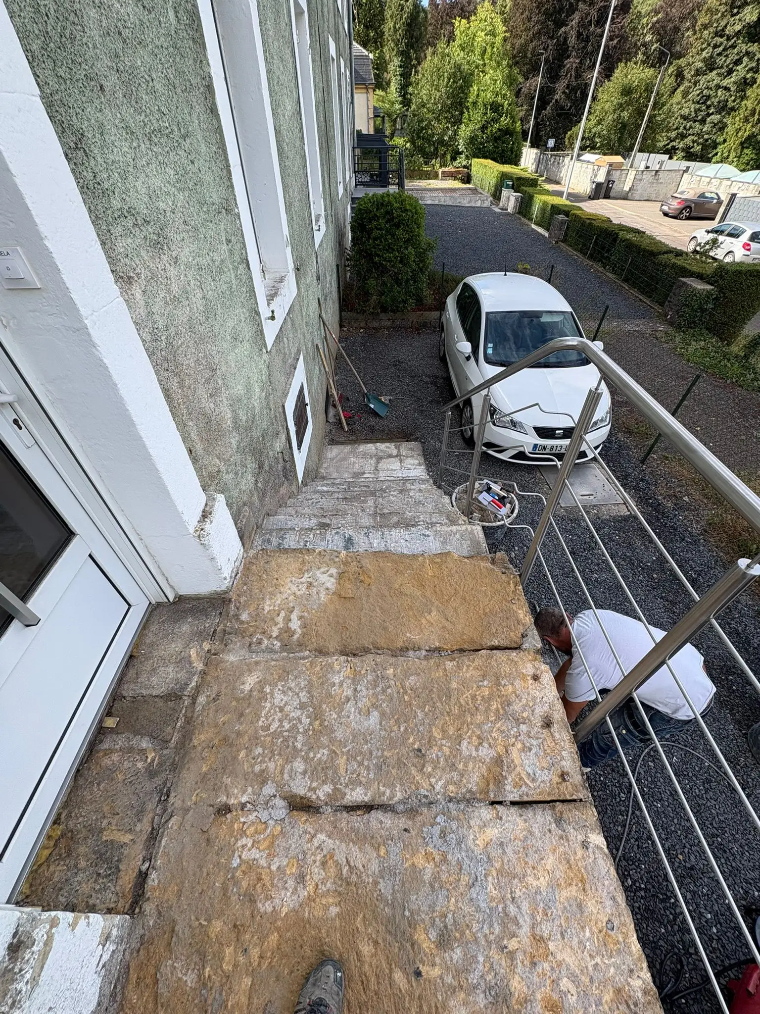 Palier d’entrée en grandes dalles de pierre jaune fissurées devant une porte blanche, avant travaux.